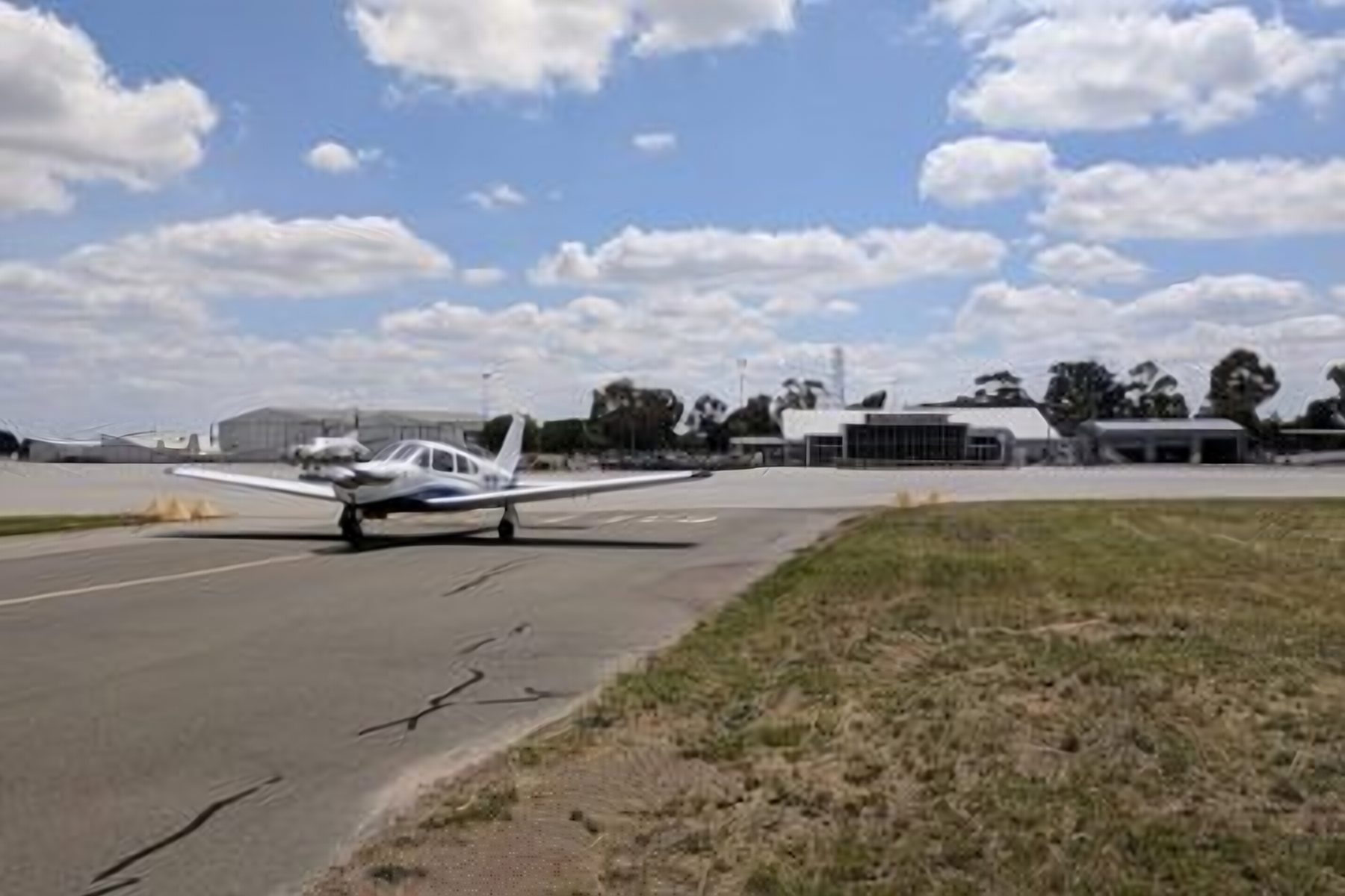 A light aircraft on an airport taxiway under a wide blue sky